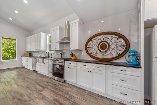 kitchen with dark countertops, appliances with stainless steel finishes, a sink, wall chimney exhaust hood, and lofted ceiling