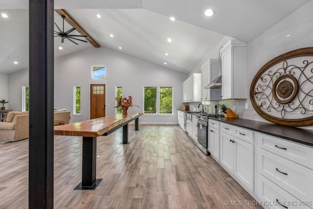 kitchen featuring dark countertops, stainless steel gas range oven, beam ceiling, light wood-style floors, and white cabinetry