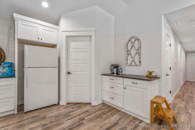 kitchen with dark countertops, freestanding refrigerator, light wood-style floors, recessed lighting, and white cabinetry