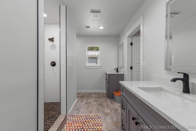 bathroom with wood finished floors, a sink, a walk in shower, and two vanities