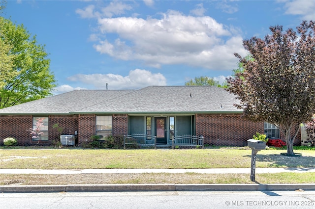 ranch-style house featuring a porch, brick siding, central AC, a front lawn, and a shingled roof