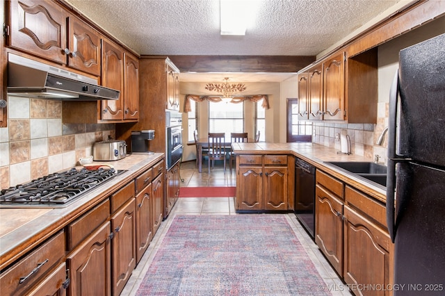 kitchen with tile countertops, a peninsula, under cabinet range hood, and black appliances