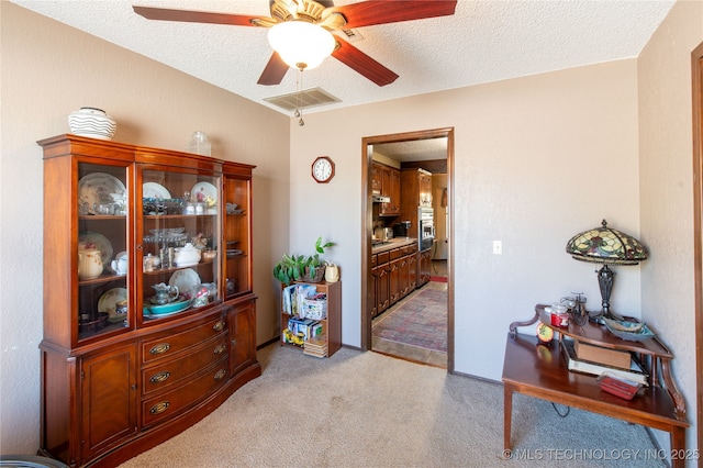 interior space featuring a textured ceiling, ceiling fan, visible vents, and light carpet