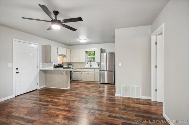 kitchen with appliances with stainless steel finishes, light countertops, a peninsula, dark wood-type flooring, and visible vents