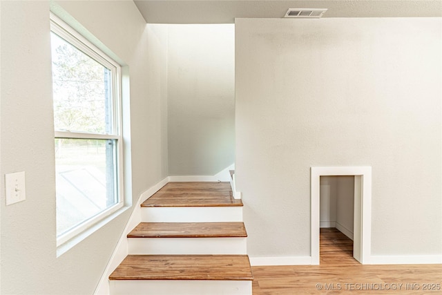 stairway with baseboards, wood finished floors, and visible vents