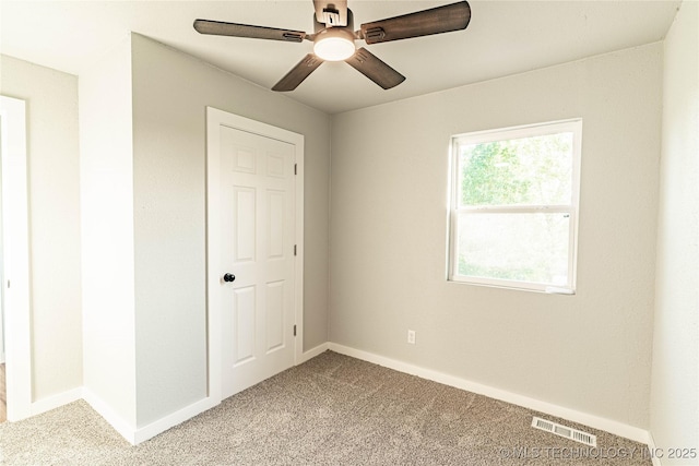 carpeted empty room featuring ceiling fan, visible vents, and baseboards
