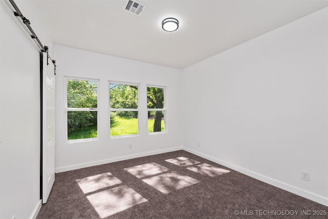 empty room with baseboards, visible vents, a barn door, and dark colored carpet