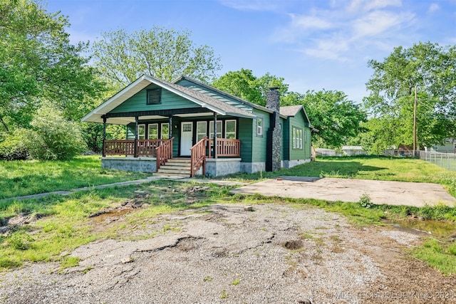 bungalow-style home featuring a front yard, fence, covered porch, and a chimney