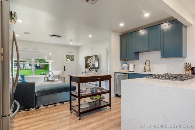 kitchen with a sink, light countertops, light wood-style flooring, stainless steel appliances, and visible vents