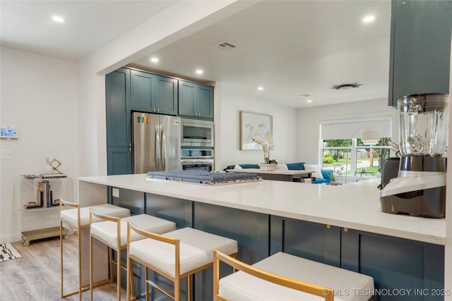 kitchen with a kitchen breakfast bar, appliances with stainless steel finishes, light wood finished floors, and a peninsula