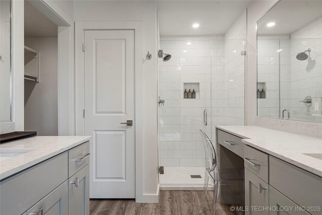 bathroom with a stall shower, wood finished floors, and two vanities