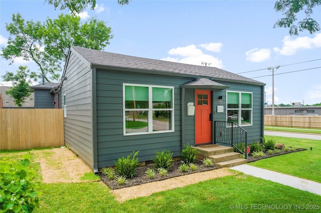 view of front of home featuring fence, a shingled roof, and a front yard