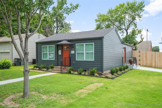 view of front of property featuring fence, a shingled roof, and a front lawn