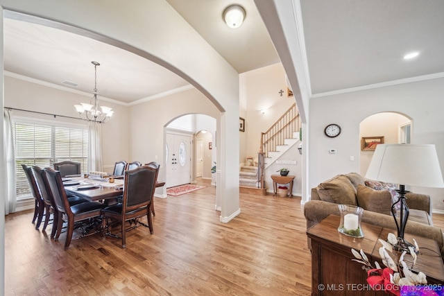 dining area with arched walkways, baseboards, a chandelier, light wood-style floors, and stairs