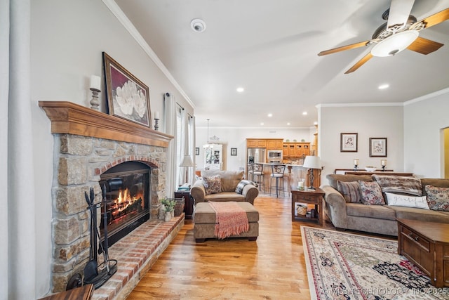 living room featuring crown molding, light wood finished floors, a stone fireplace, a ceiling fan, and recessed lighting