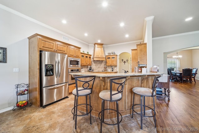 kitchen featuring light stone countertops, ornamental molding, stainless steel appliances, a peninsula, and custom exhaust hood