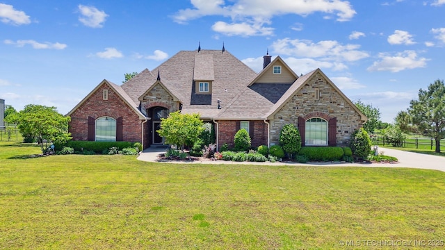 french country inspired facade with stone siding, fence, and a front yard