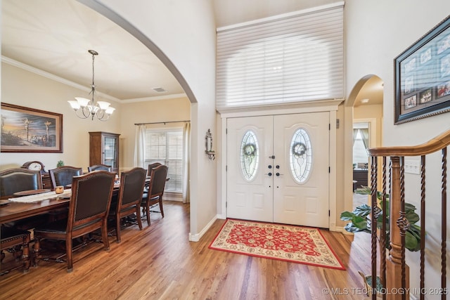 foyer featuring a towering ceiling, visible vents, light wood-type flooring, a notable chandelier, and ornamental molding