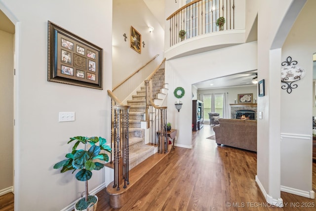 foyer entrance featuring wood finished floors, baseboards, ceiling fan, a lit fireplace, and arched walkways