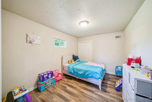 bedroom with baseboards, visible vents, wood finished floors, and a closet