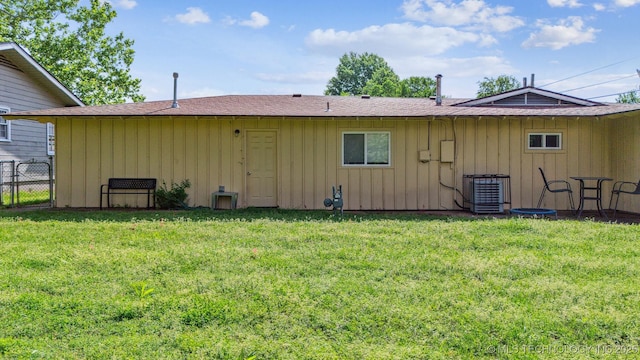 rear view of property with a lawn, board and batten siding, central air condition unit, and fence