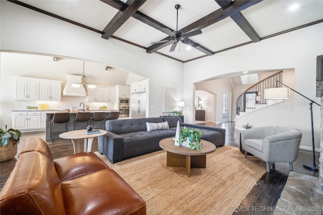 living room featuring a ceiling fan, arched walkways, stairway, light wood-style floors, and coffered ceiling