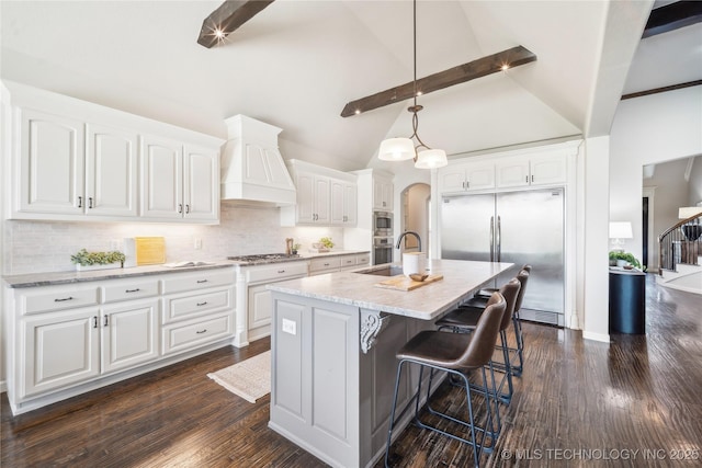 kitchen with backsplash, a sink, premium range hood, white cabinets, and built in appliances