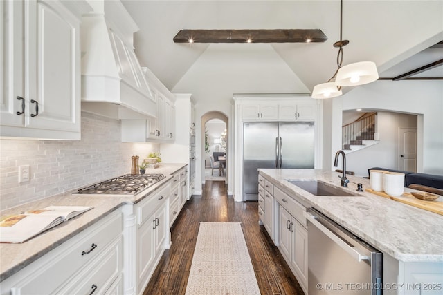 kitchen with arched walkways, a sink, premium range hood, white cabinets, and stainless steel appliances
