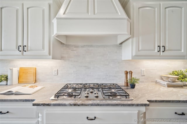 kitchen with decorative backsplash, stainless steel gas cooktop, light stone counters, white cabinets, and custom exhaust hood
