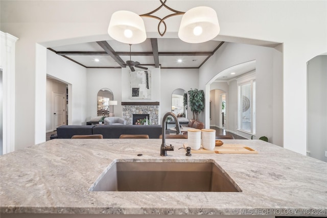 kitchen featuring a sink, light stone counters, ceiling fan, and coffered ceiling