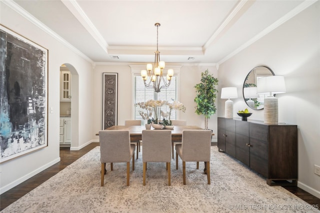 dining room with an inviting chandelier, crown molding, wood finished floors, a tray ceiling, and arched walkways