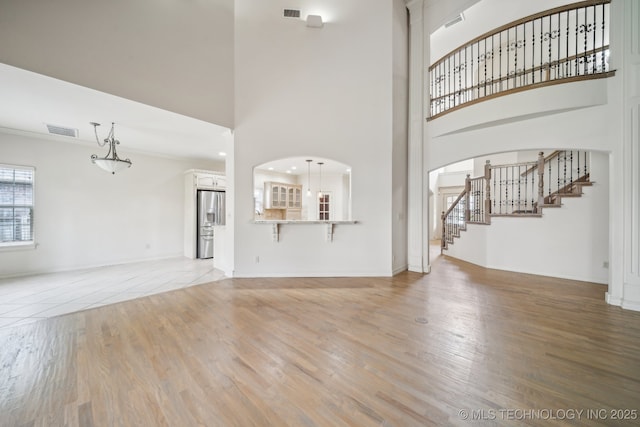 8655 E 103rd St, Tulsa, OK 74133 - unfurnished living room featuring a high ceiling, stairway, arched walkways, light wood finished floors, and baseboards