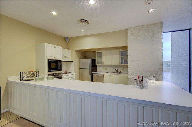 kitchen with appliances with stainless steel finishes, a sink, light countertops, under cabinet range hood, and visible vents