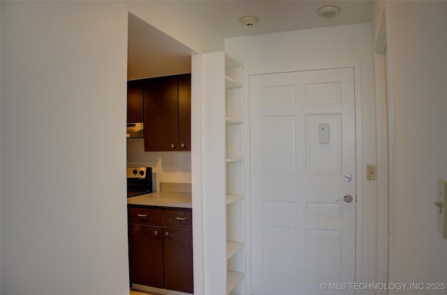 interior space with dark brown cabinetry, range, open shelves, light countertops, and under cabinet range hood
