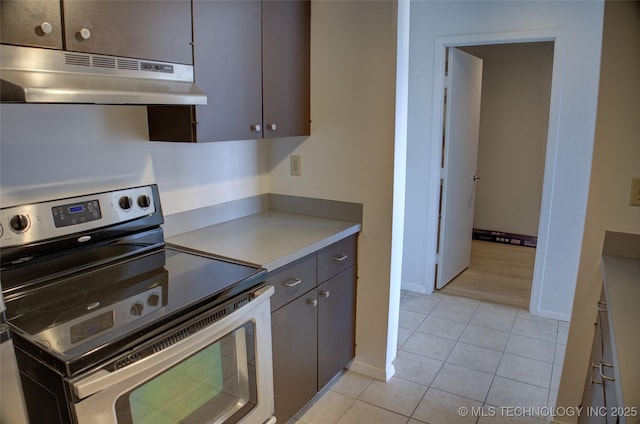 kitchen with light countertops, electric stove, baseboards, light tile patterned floors, and under cabinet range hood