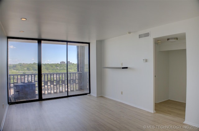 empty room with baseboards, visible vents, expansive windows, and wood finished floors