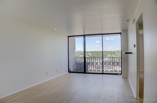 unfurnished room featuring a wall of windows, baseboards, wood finished floors, and visible vents