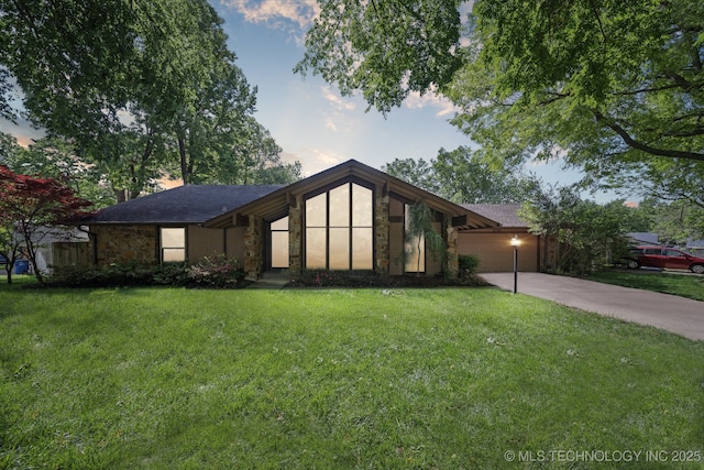 mid-century home featuring a garage, driveway, a front lawn, and stone siding