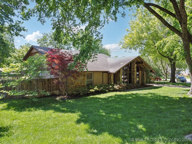 exterior space featuring a lawn, fence, and stone siding