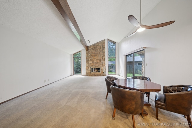 dining area with ceiling fan, lofted ceiling with beams, a stone fireplace, and light colored carpet