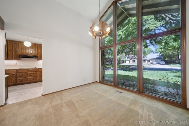 unfurnished dining area with light colored carpet, an inviting chandelier, high vaulted ceiling, baseboards, and visible vents