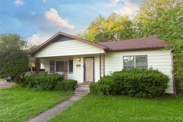 view of front facade with roof with shingles, covered porch, and a front yard