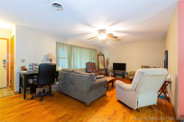 living area with a textured ceiling, a ceiling fan, light wood-style flooring, and visible vents