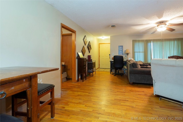 living room with a ceiling fan, light wood-type flooring, and a textured ceiling
