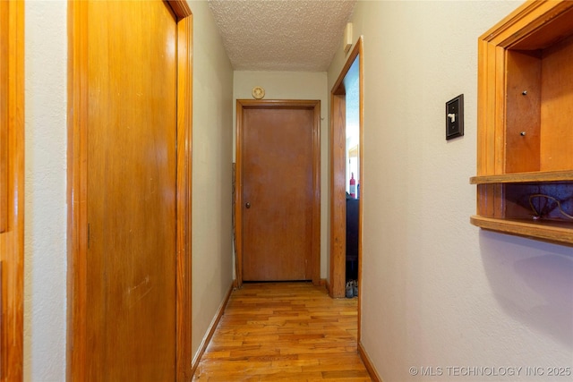 hall with baseboards, a textured ceiling, and light wood-style flooring