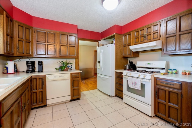 kitchen featuring white appliances, under cabinet range hood, brown cabinetry, and light countertops