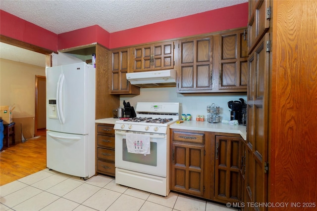 kitchen with brown cabinetry, white appliances, light countertops, a textured ceiling, and under cabinet range hood