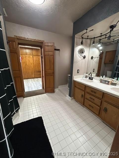 bathroom featuring a sink, double vanity, a textured ceiling, and tile patterned floors