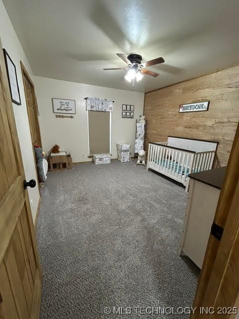 bedroom featuring carpet floors, ceiling fan, wood walls, and a crib