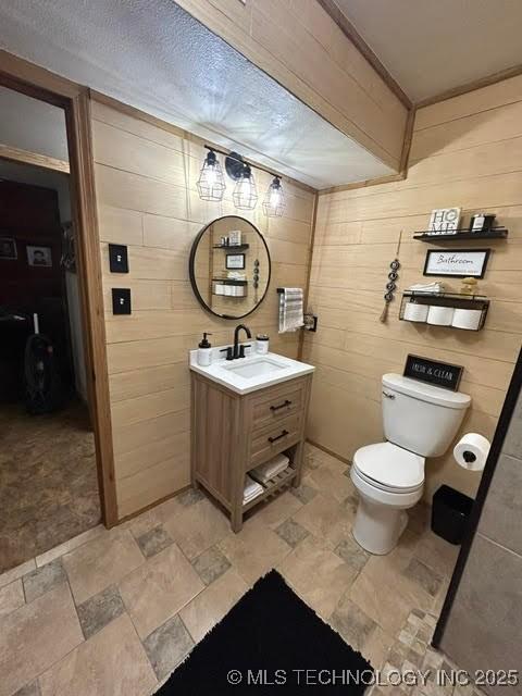 bathroom with wooden walls, toilet, stone finish floor, and vanity